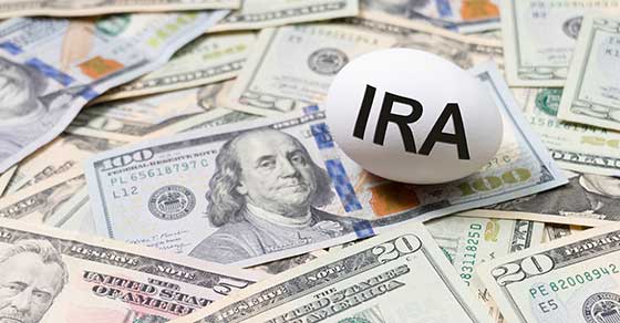 Nest egg with IRA written on it on laying across a stack of bills