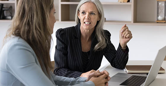 A female manager sitting with an employee working on their laptop talking about performance