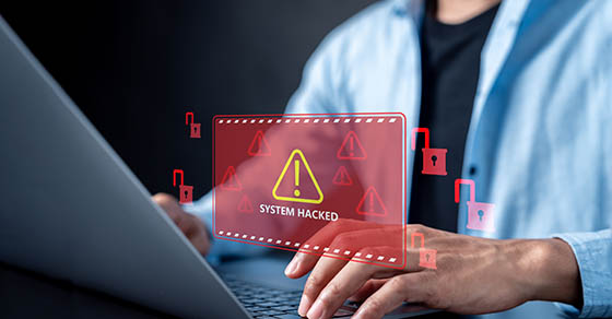 Individual typing on a laptop with a screen alert that the system has been hacked